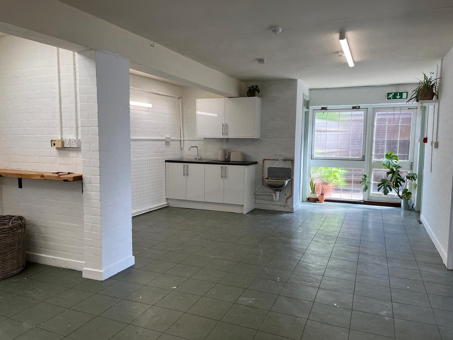 Empty interior at Dolphin House Arts, with white brick walls, a kitchenette and glazed entrance doors